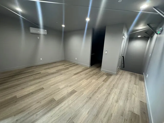 Spacious room featuring wood-finish flooring, recessed lighting, a modern mini-split HVAC unit, and neutral gray walls