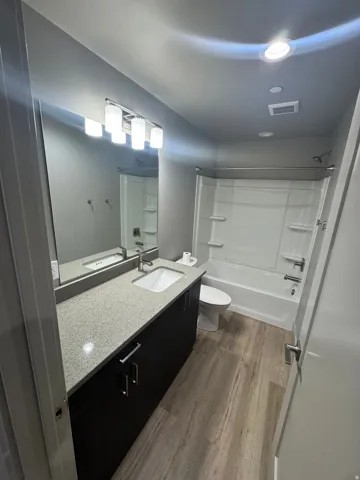 Contemporary bathroom featuring a single vanity with dark cabinetry, a light speckled countertop, and an integrated rectangular sink