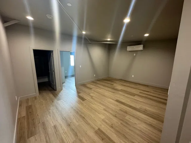 Spacious room featuring wood-finish flooring, recessed ceiling lighting, and a wall-mounted mini-split HVAC unit