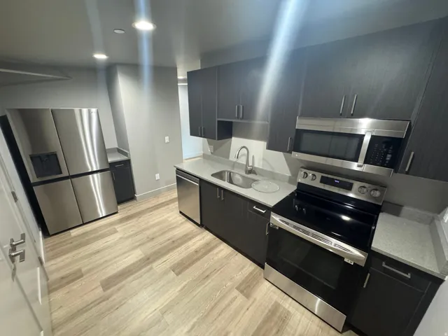 Contemporary kitchen featuring dark wood-finish cabinetry, stainless steel appliances, light gray countertops, recessed lighting, and wood-finish flooring