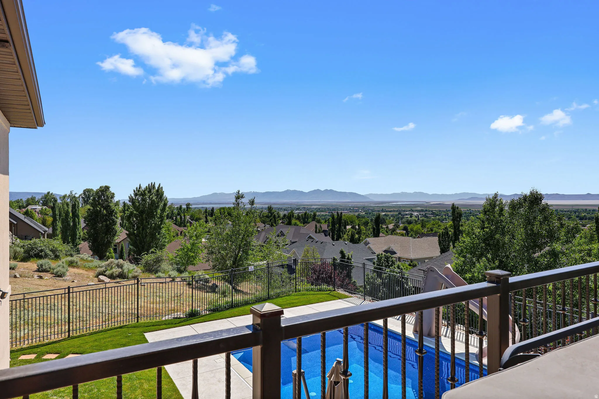 Outdoor living space featuring a swimming pool with integrated slide, concrete patio, and wrought iron railing