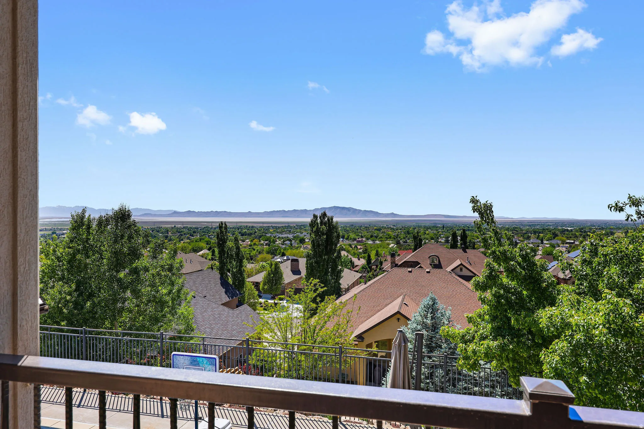 Expansive outdoor space featuring a dark wood-finish railing with black balusters, overlooking distant mountains and a residential landscape with mature trees
