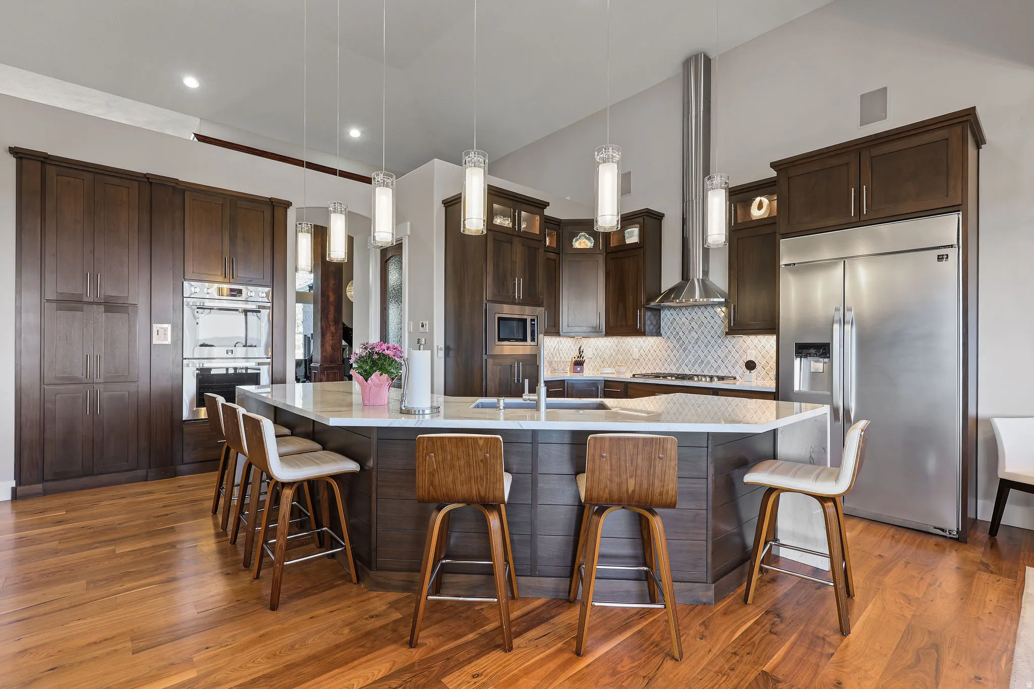 Kitchen featuring a central island with countertop seating, rich wood-finish cabinetry, built-in stainless steel appliances, a tile backsplash, and wood-finish flooring