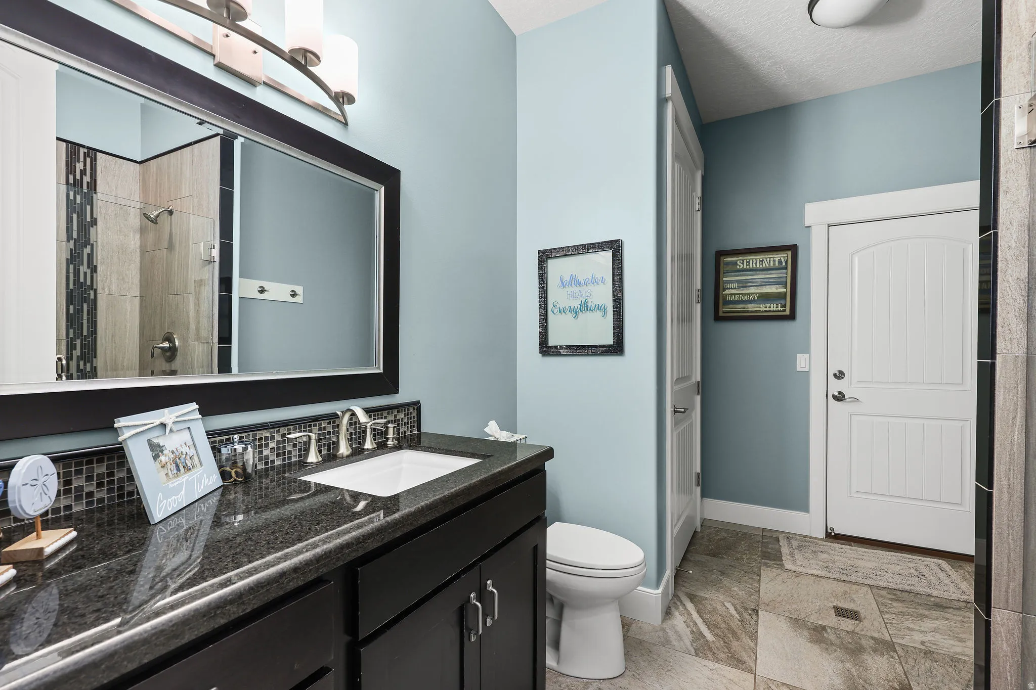 Vanity featuring a dark countertop, undermount sink, and mosaic tile backsplash
