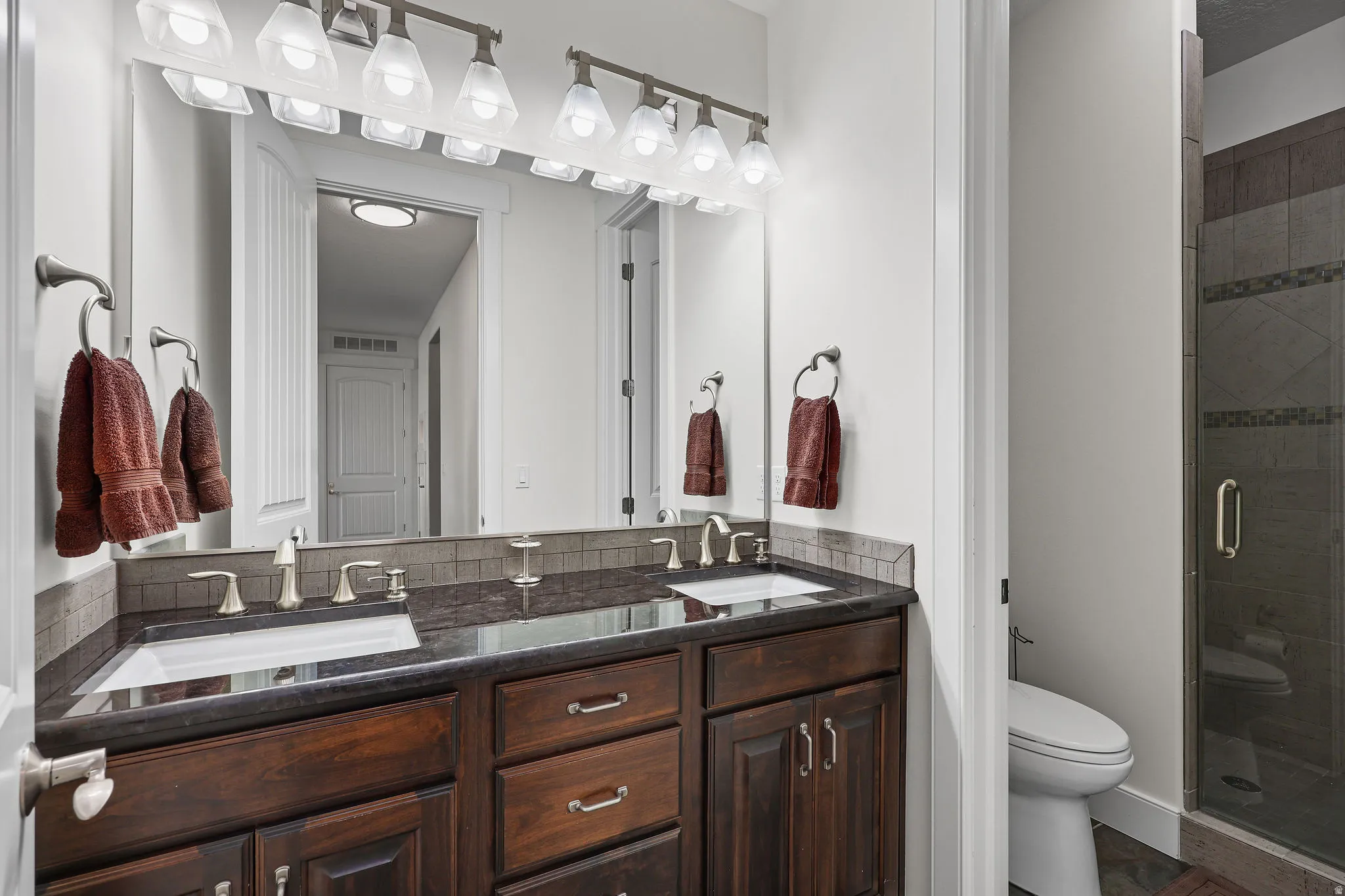 Double vanity featuring dark wood cabinetry, dual undermount sinks, and a dark countertop with a tiled backsplash
