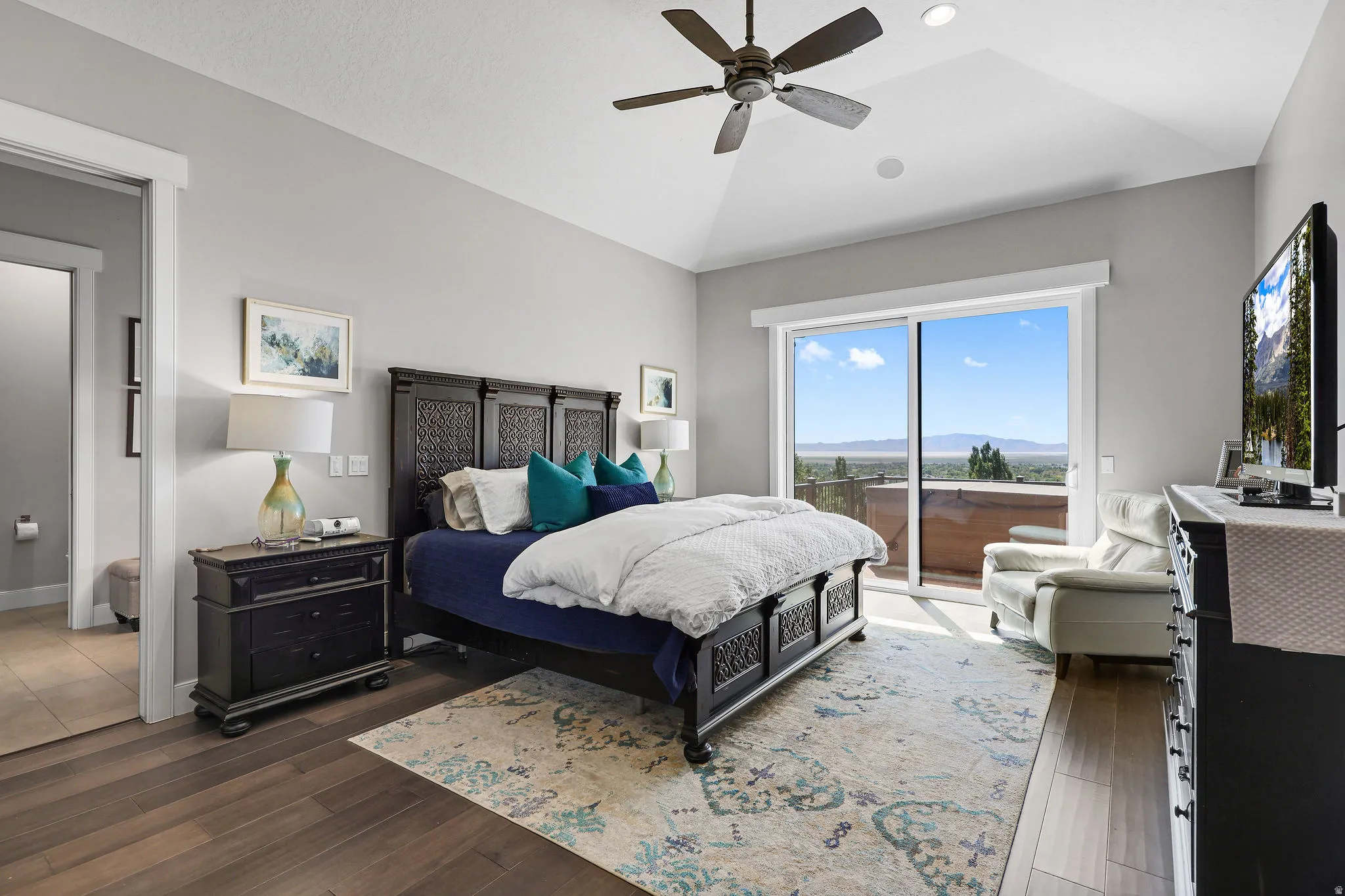 Vaulted ceiling bedroom with a ceiling fan, wood-finish flooring, and sliding glass doors opening to a balcony