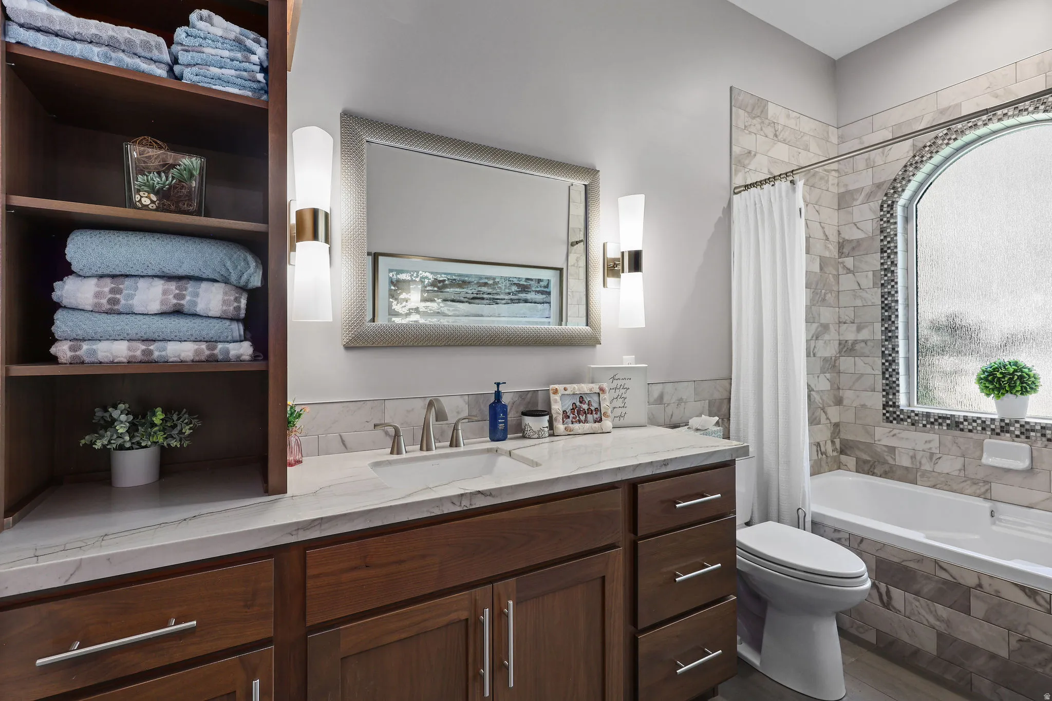 Bathroom featuring a single vanity with wood-finish cabinetry and a white countertop, an undermount sink, and a framed mirror with integrated sconce lighting