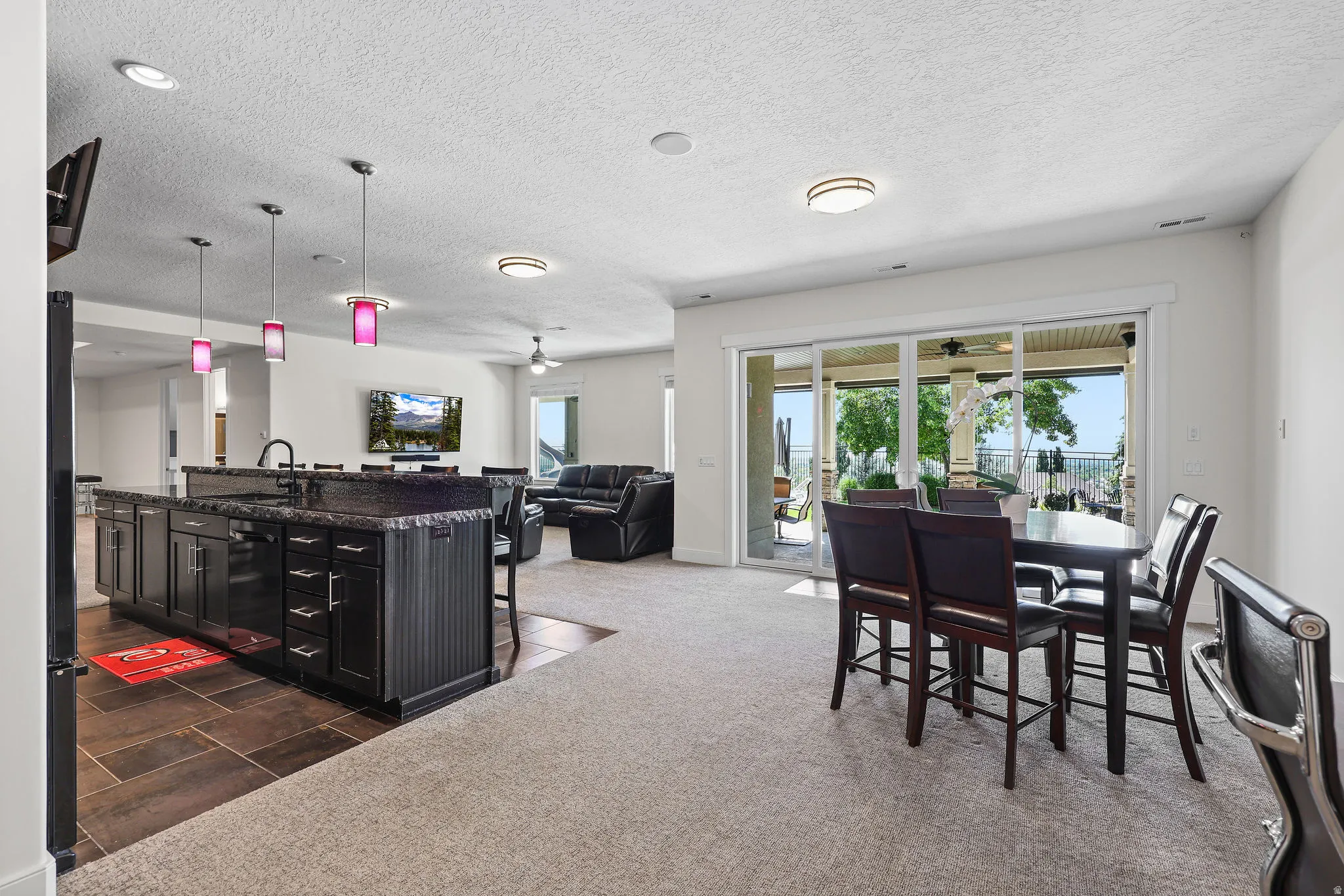 Spacious open-concept recreation room featuring a large kitchen island with dark cabinetry and a stone-finish countertop, a built-in sink with a gooseneck faucet, and recessed lighting