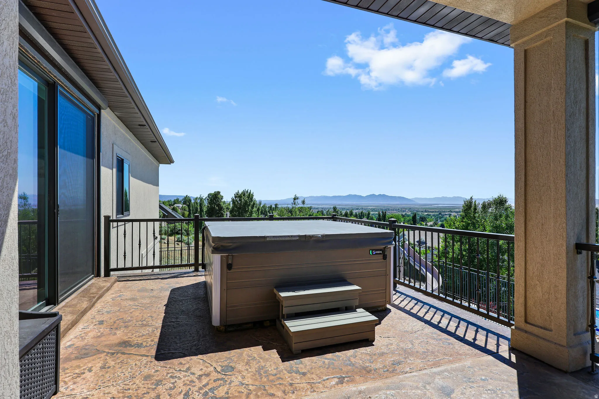 Expansive exterior balcony featuring a hot tub, stamped concrete flooring, and black metal railing