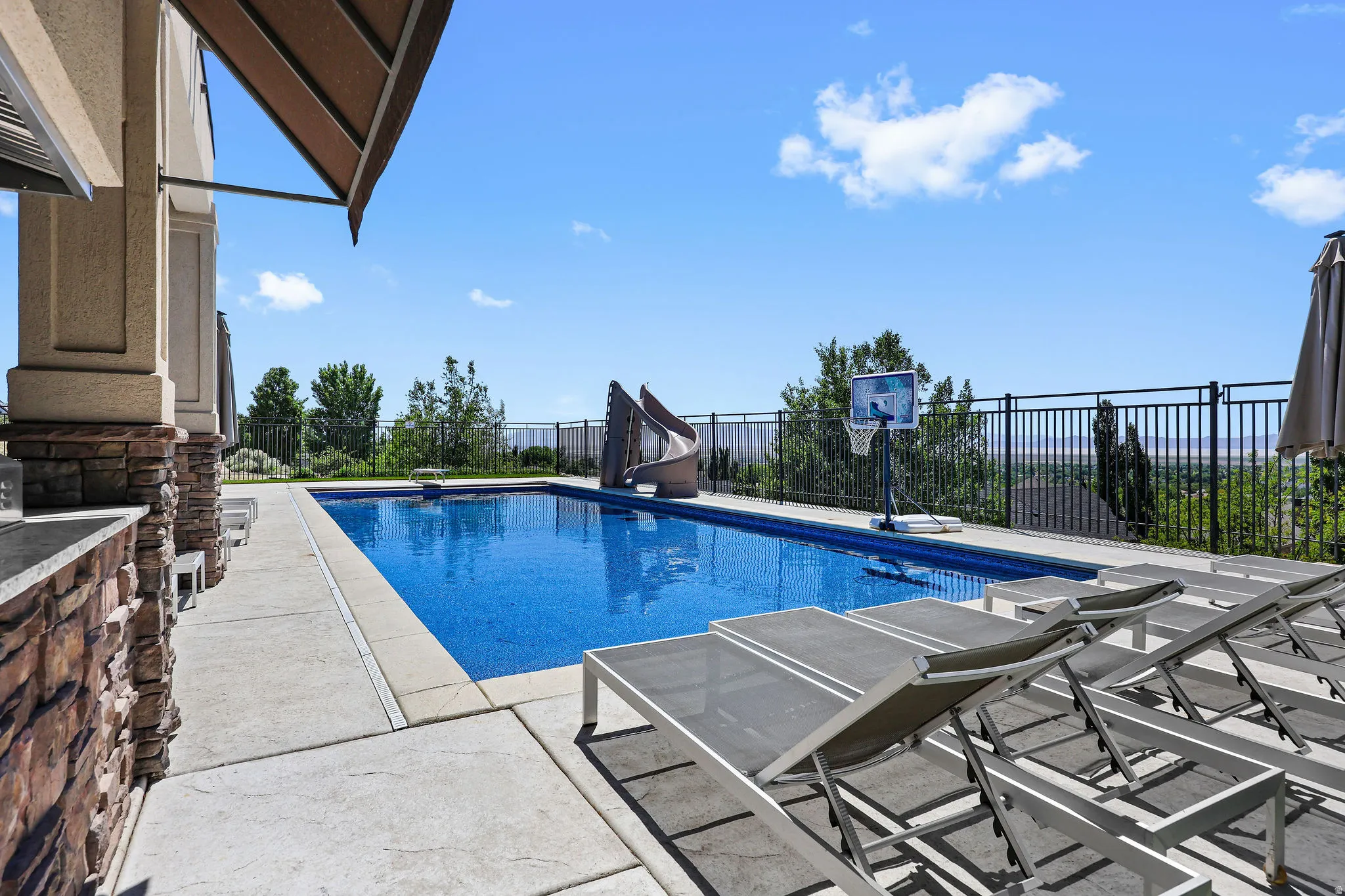 Expansive outdoor space featuring a rectangular swimming pool, concrete patio, and a stone-clad outdoor kitchen area with an integrated countertop