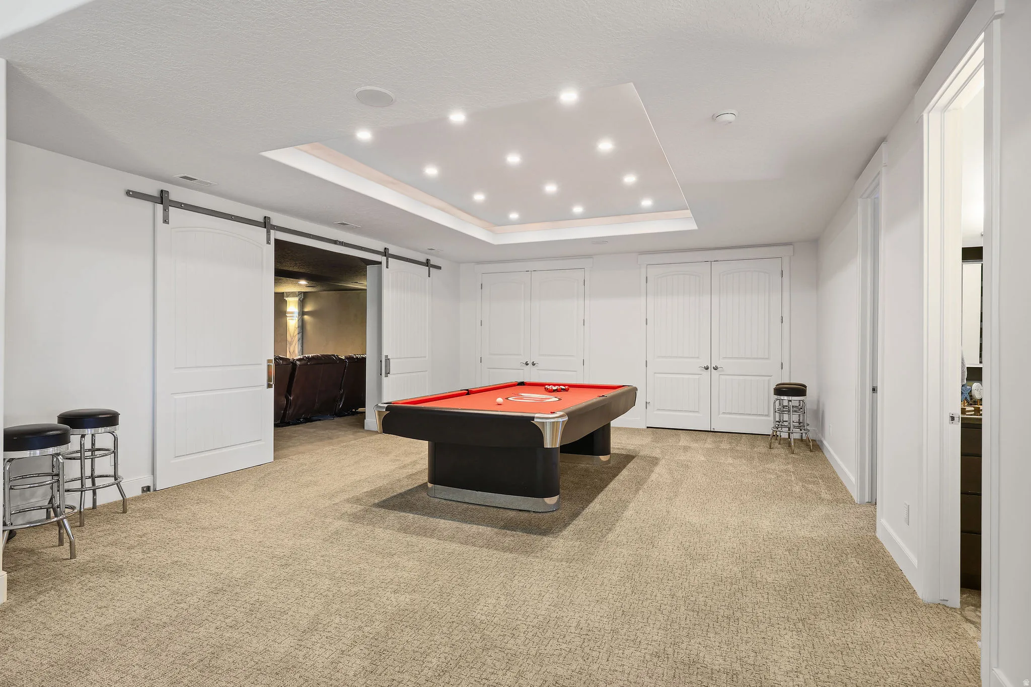 Spacious recreation area featuring plush carpeting, a recessed ceiling with abundant lighting, and a barn door entry