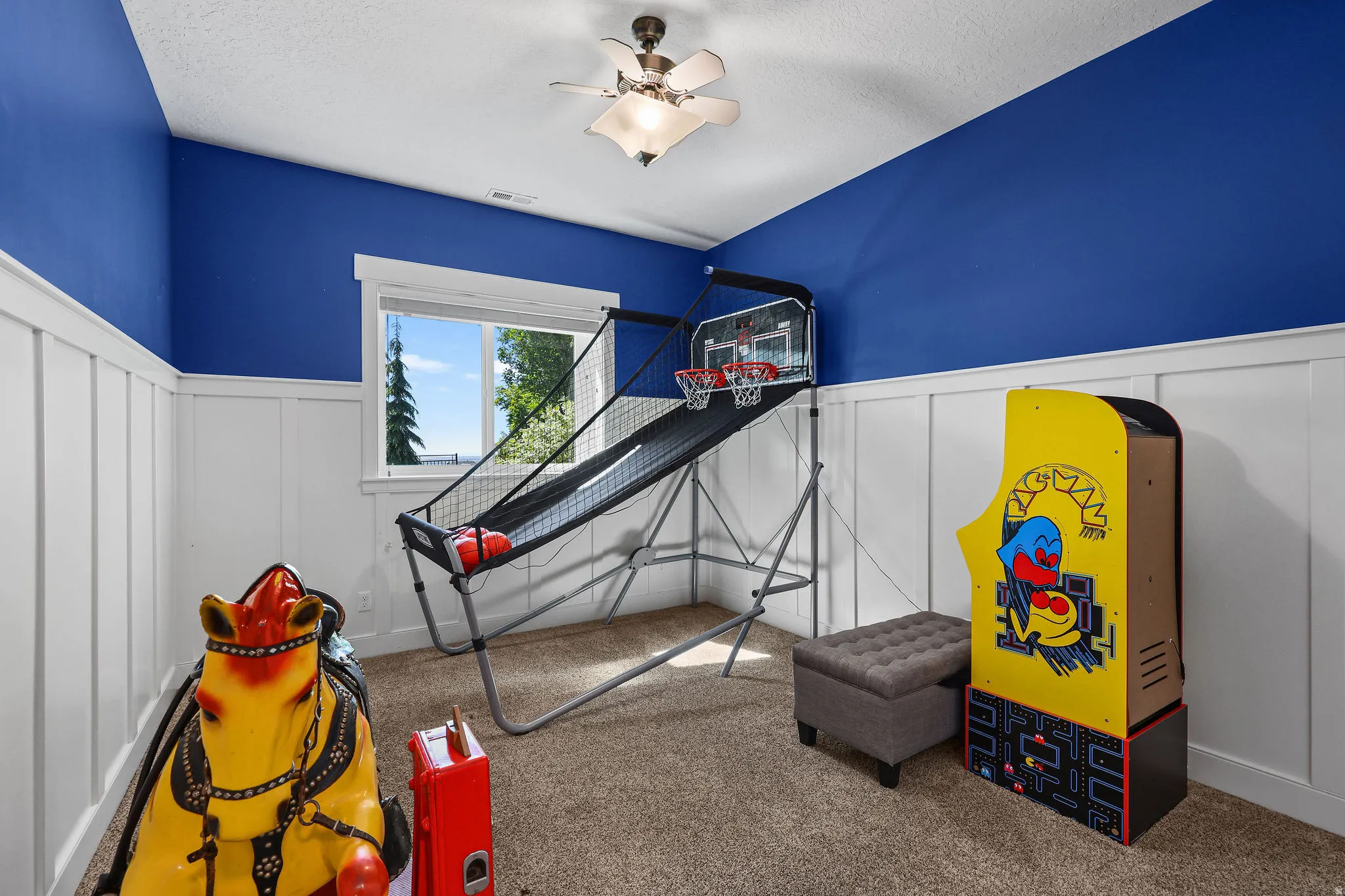 Room featuring board and batten wainscoting with a vibrant blue wall above, a window with white trim, and a ceiling fan with integrated lighting