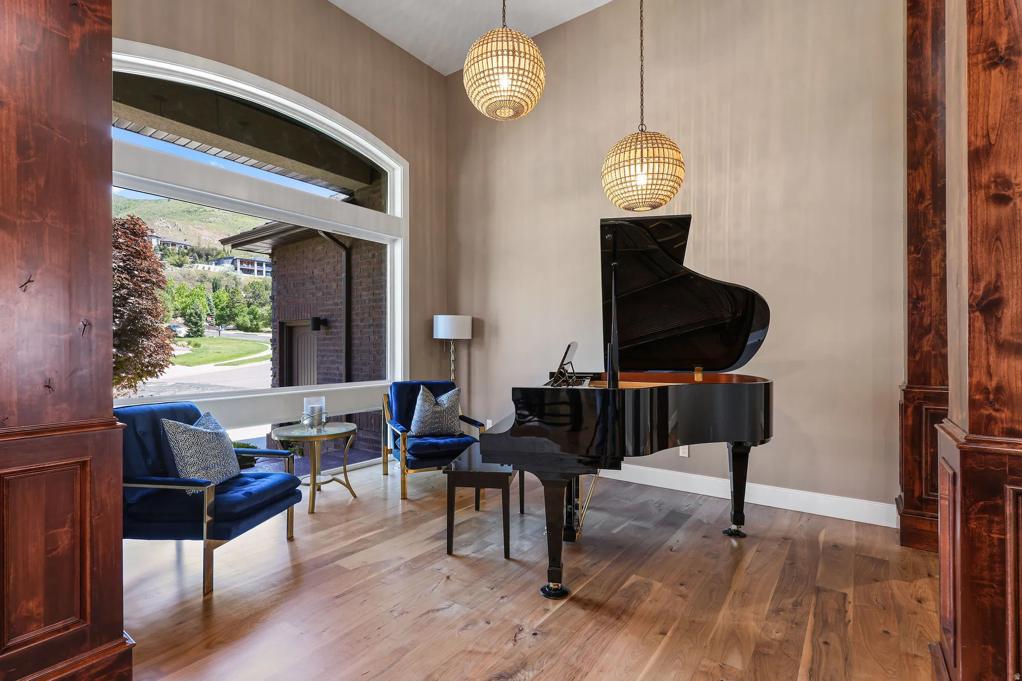 Arched window framing mountain scenery, complemented by wood-finish flooring, accent walls, and dual pendant lighting fixtures