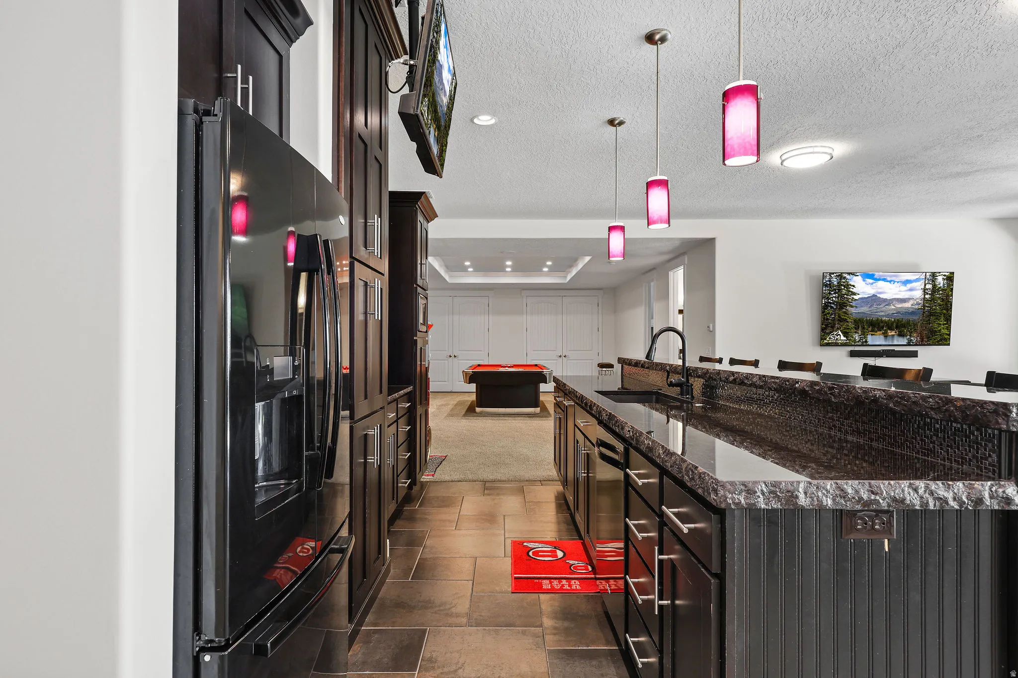 Spacious entertainment area featuring a full-size refrigerator, dark wood cabinetry, and a substantial island with a dark granite countertop and integrated sink