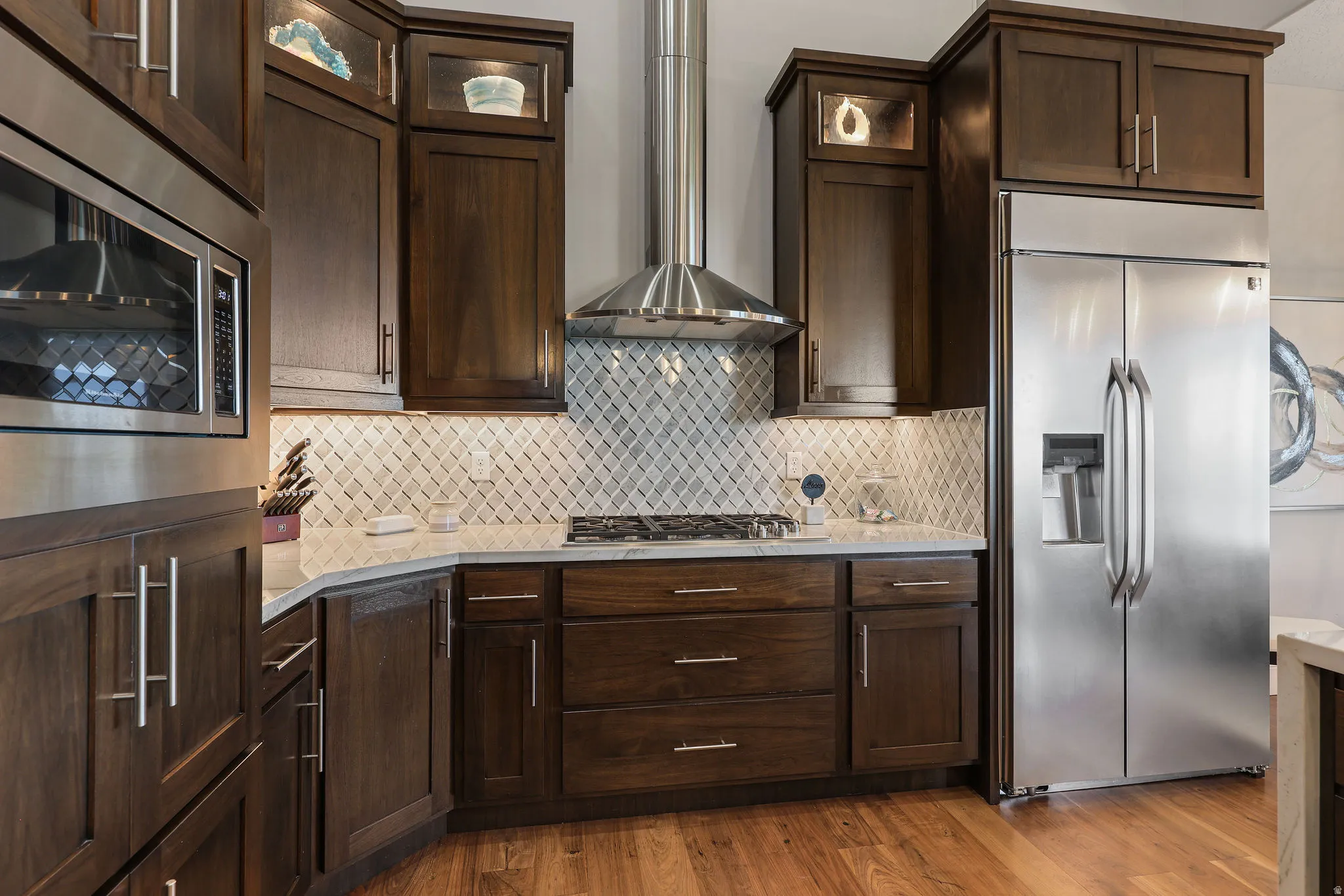 Kitchen featuring dark wood cabinetry, a stainless steel gas range with a matching range hood, a built-in stainless steel microwave, a stainless steel side-by-side refrigerator, and light-colored countertops with a diamond-patterned backsplash