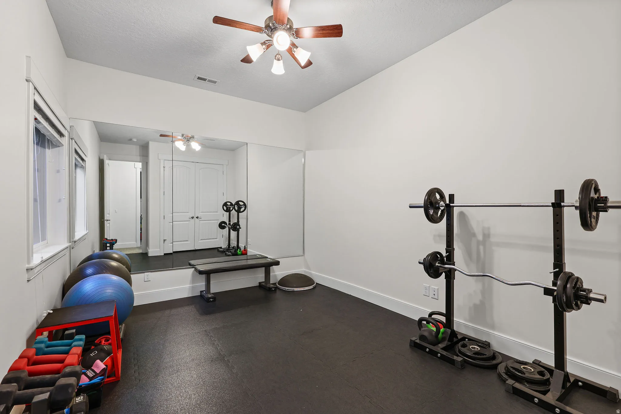 Dedicated exercise room featuring dark rubber flooring, expansive wall-mounted mirrors, and an angled ceiling