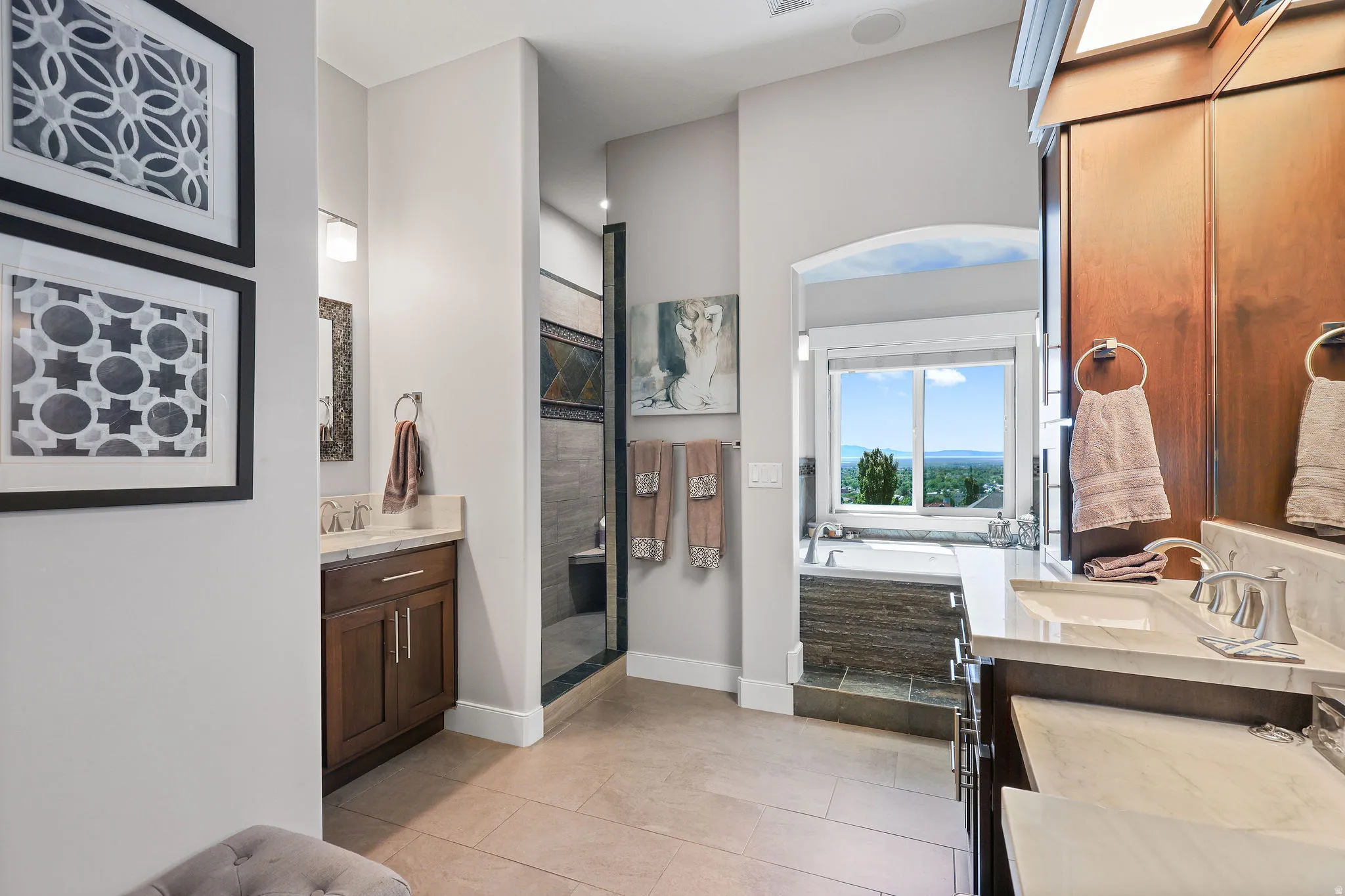 Bathroom featuring dual vanities with integrated sinks, a walk-in shower with decorative tile, a built-in soaking tub, and tile flooring