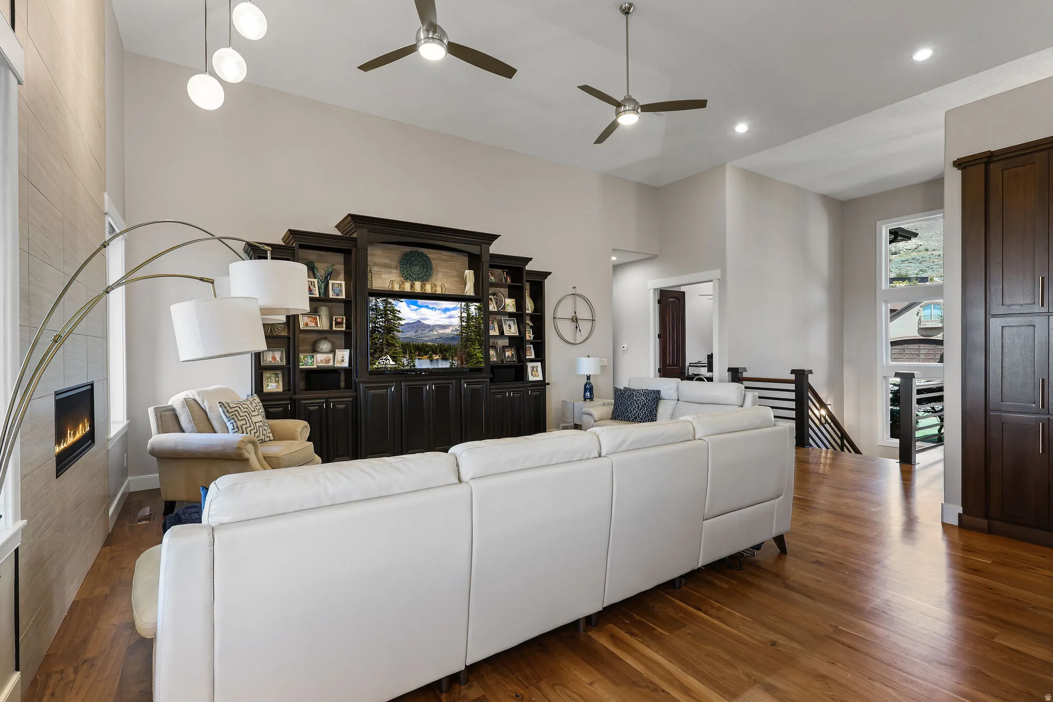 Spacious living area featuring high vaulted ceilings, recessed lighting, wood-finish flooring, a built-in media center with shelving, and a linear fireplace with a textured surround