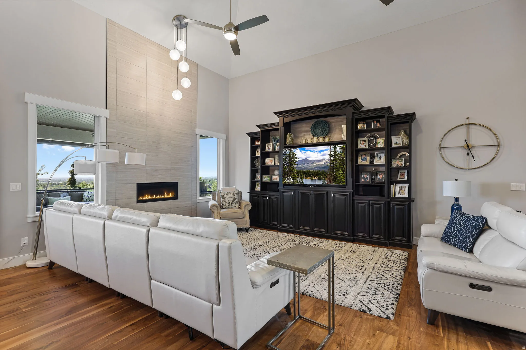 Spacious living area featuring high ceilings, wood-finish flooring, and a linear fireplace set into a floor-to-ceiling tile accent wall