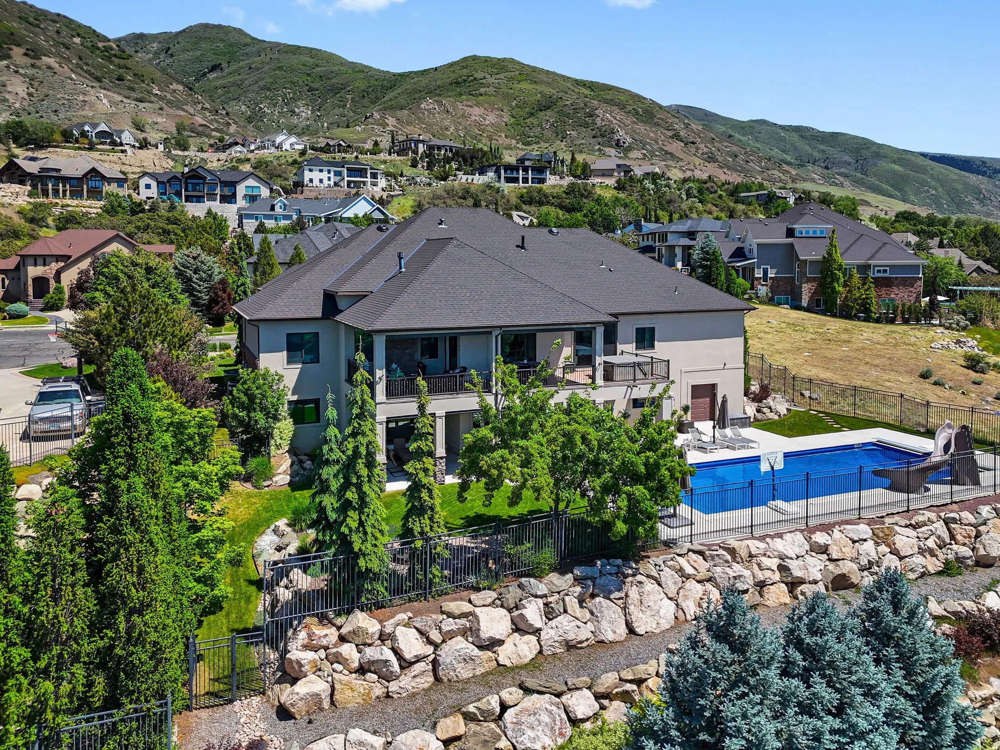 Stucco exterior residence featuring a dark shingle roof, multiple balconies, an in-ground swimming pool, and a rock retaining wall
