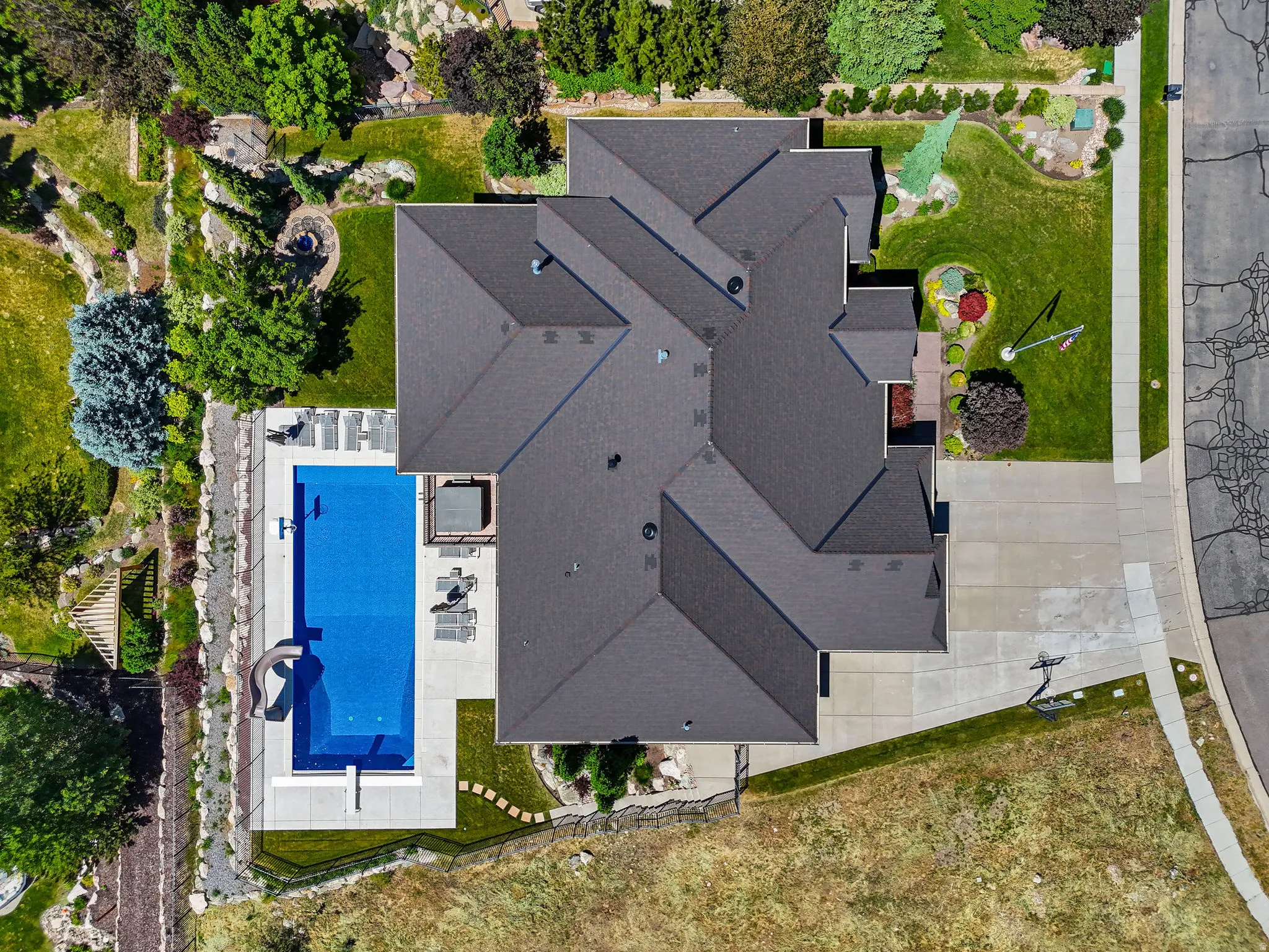 Expansive property featuring a multi-gabled roofline, concrete driveway, and a rectangular swimming pool with a slide