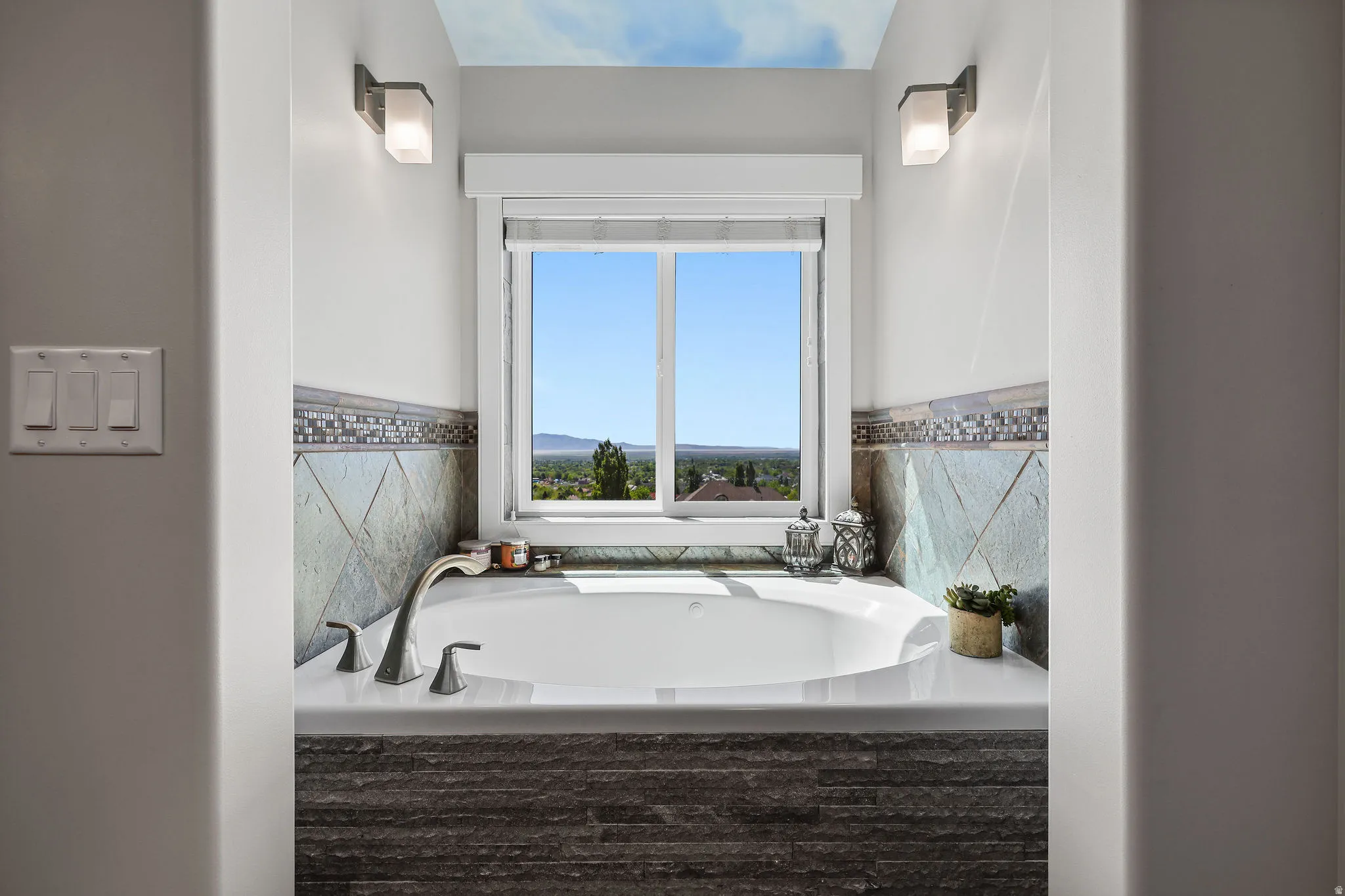 Built-in soaking tub with brushed nickel fixtures, bordered by a tiled surround featuring a mosaic accent strip
