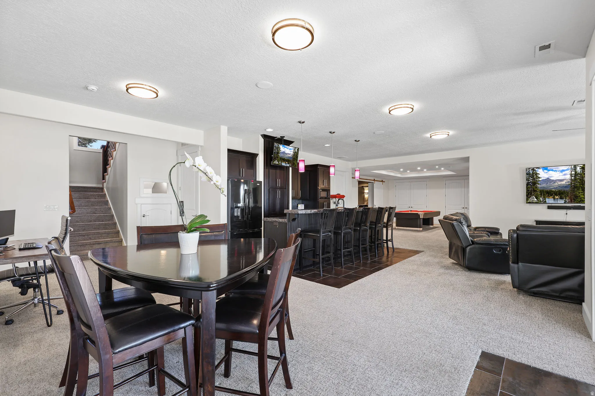 Expansive recreation room featuring a built-in wet bar with pendant lighting, integrated cabinetry, and dark tile flooring