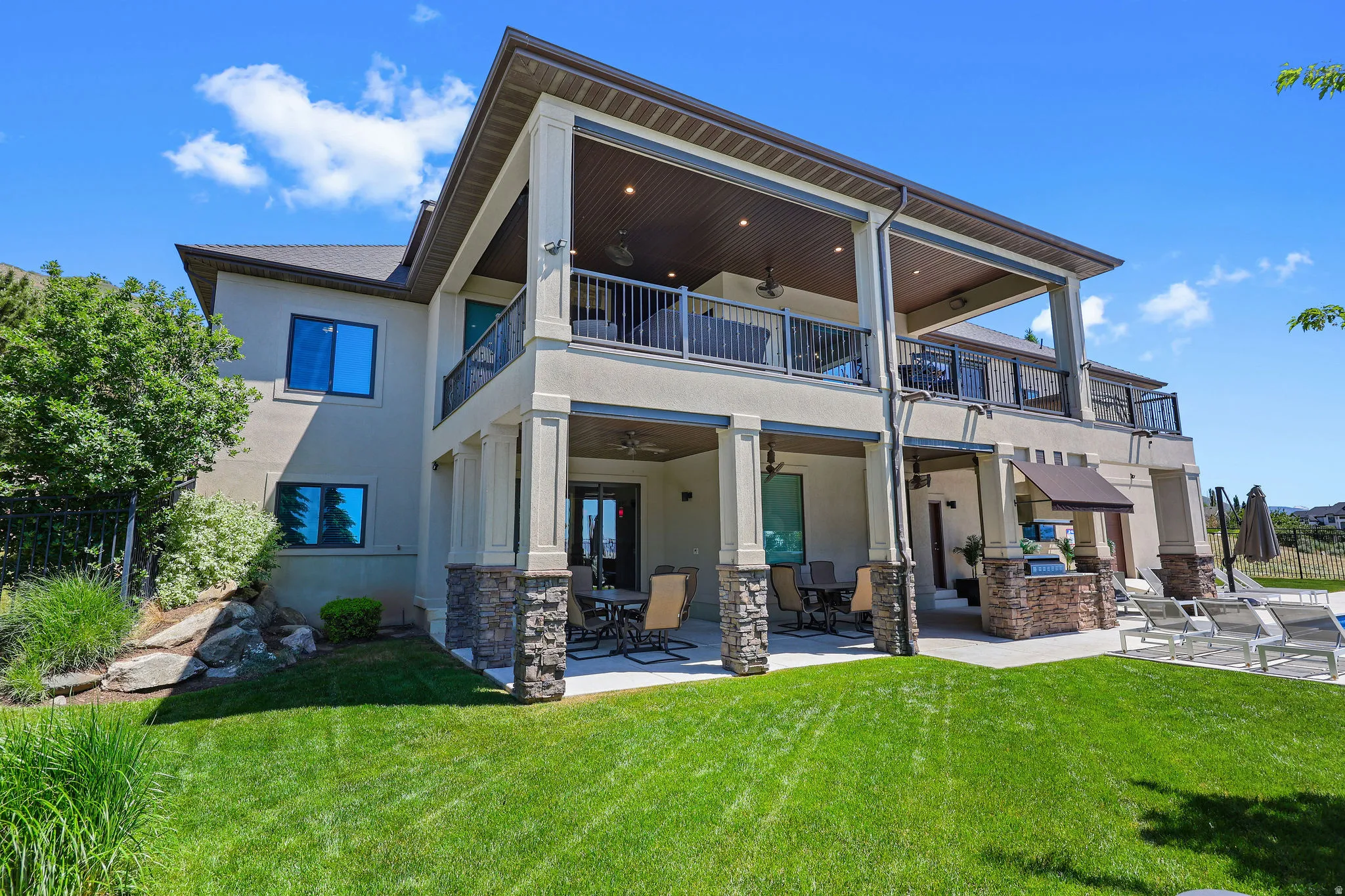 Multi-level exterior featuring covered patios, covered balconies with wrought iron railings, and stone-clad columns