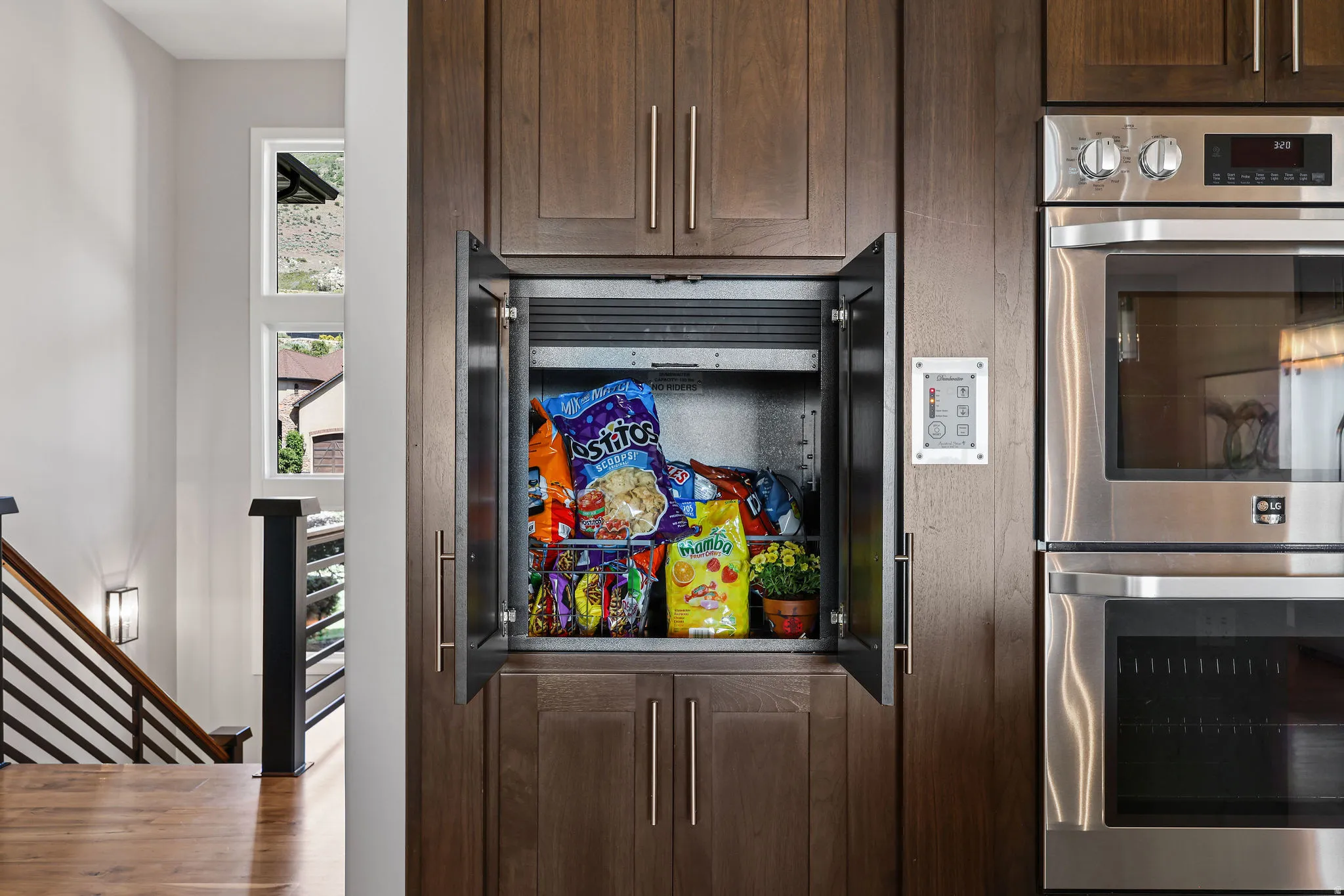 Built-in pantry storage with wood-finish cabinetry, integrated wall ovens, and contemporary stair railing with horizontal balusters