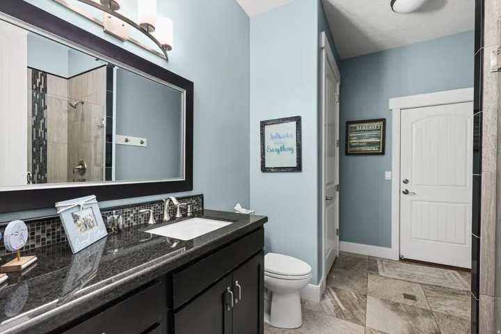 Vanity featuring a dark countertop, undermount sink, and mosaic tile backsplash
