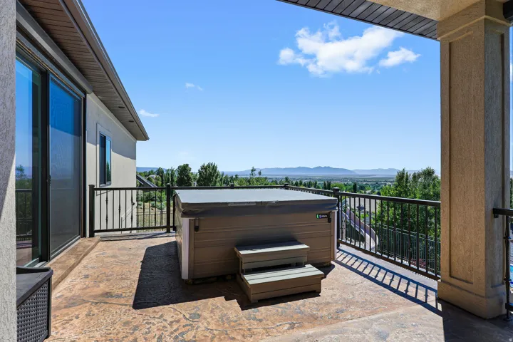 Expansive exterior balcony featuring a hot tub, stamped concrete flooring, and black metal railing