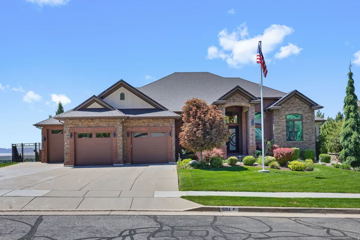 Stone and brick exterior featuring a multi-car garage with individual doors, a concrete driveway, a manicured lawn, and mature landscaping
