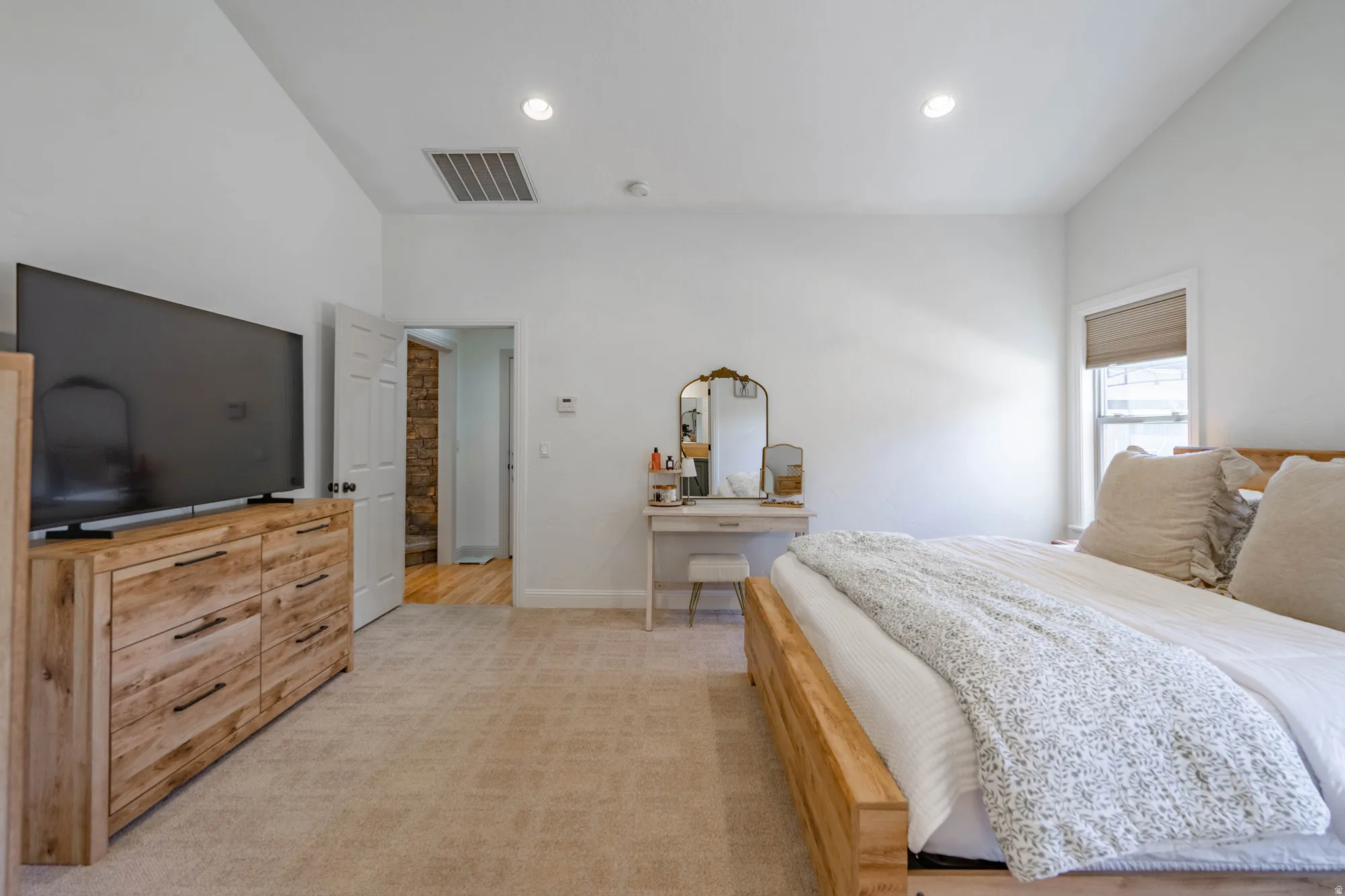 Spacious room featuring vaulted ceilings, recessed lighting, wall-to-wall carpeting, and a window with a roller shade