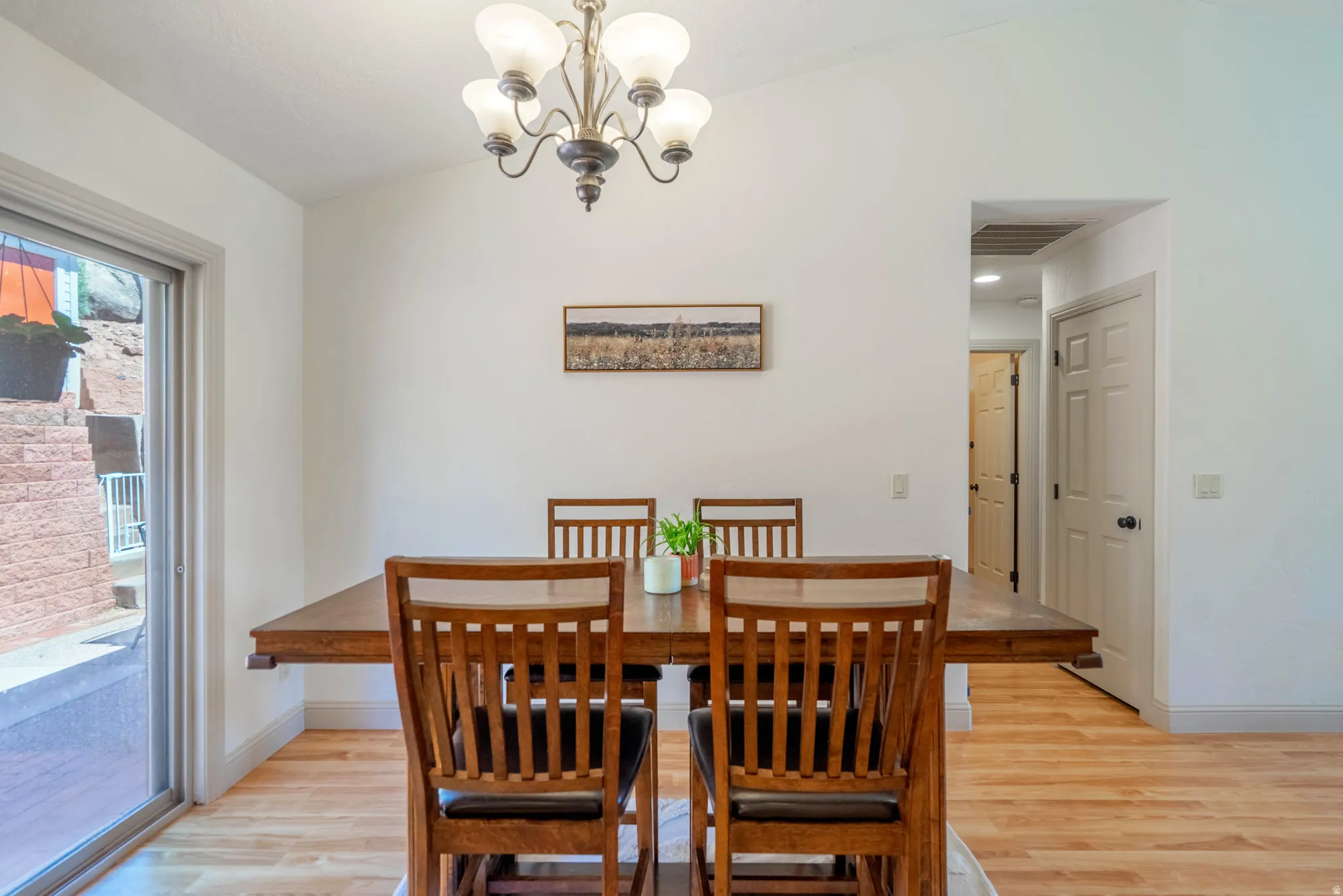 Vaulted ceiling dining area featuring light wood-finish flooring, a contemporary chandelier, and a sliding glass door