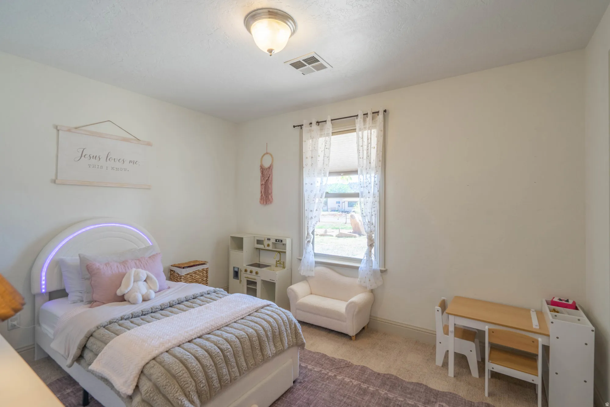 Neutral-toned room featuring a single window with sheer drapes, light-colored carpeting, and a flush-mount ceiling light
