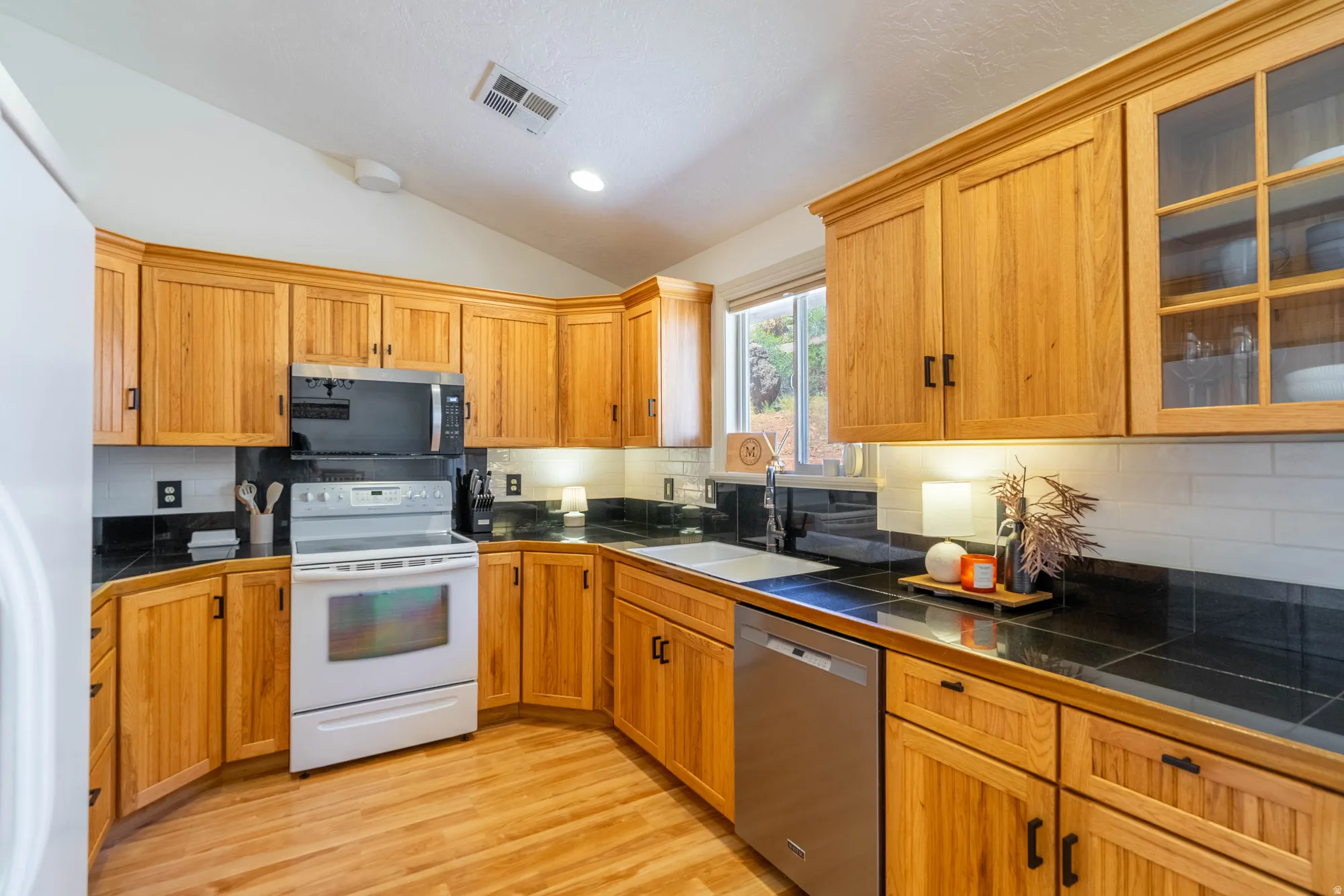 Kitchen featuring natural wood cabinetry, black countertops, and a white tile backsplash