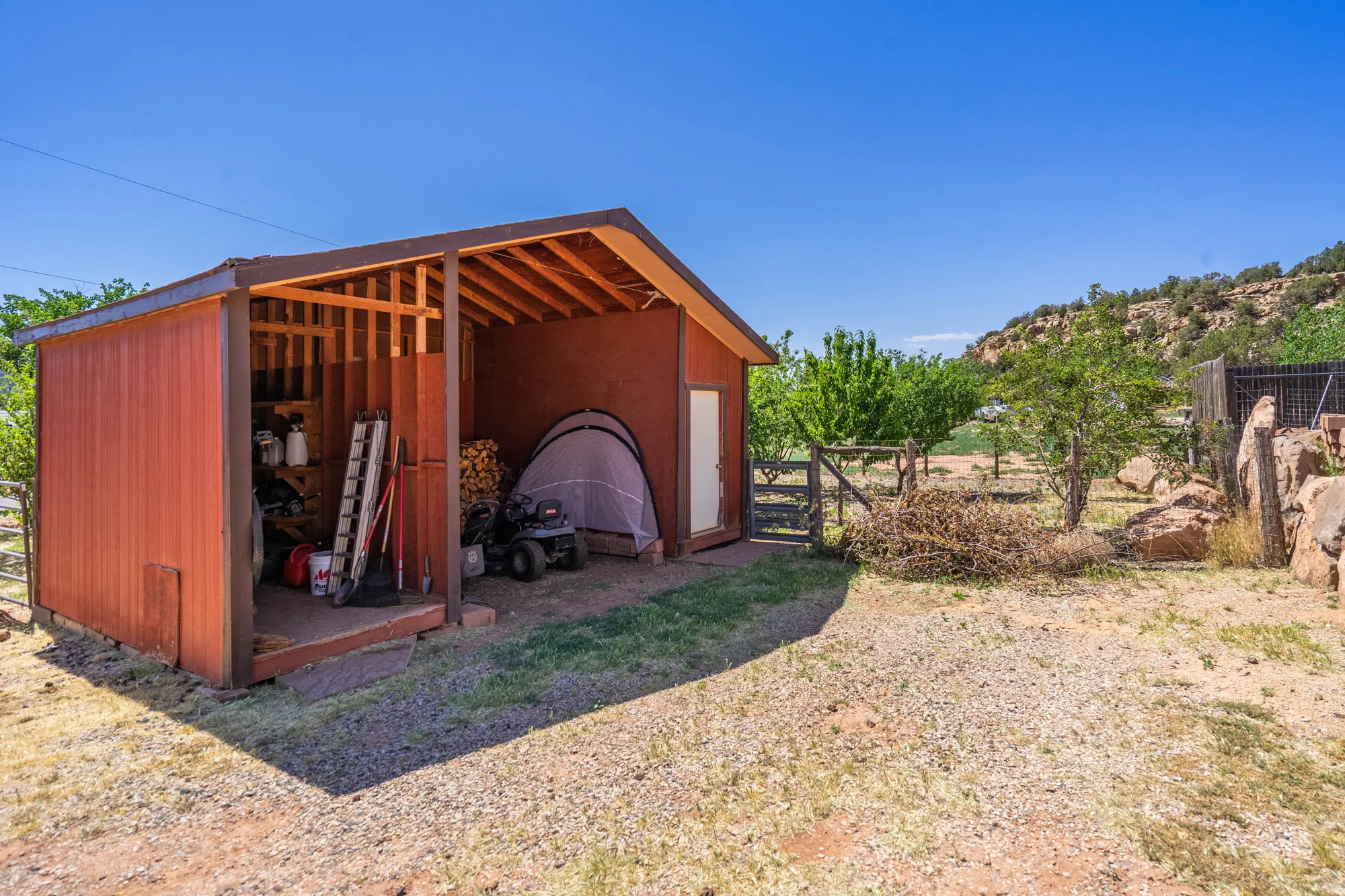 Exterior storage shed featuring a covered open-air section, a fully enclosed section with a white door, and an exposed wood frame ceiling
