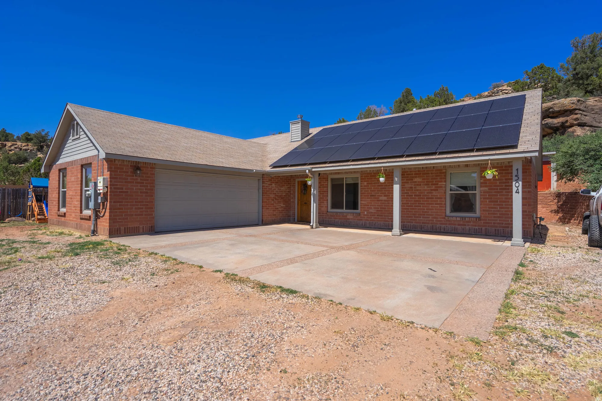Brick exterior with a large front porch, solar panel array, two-car garage, and concrete driveway