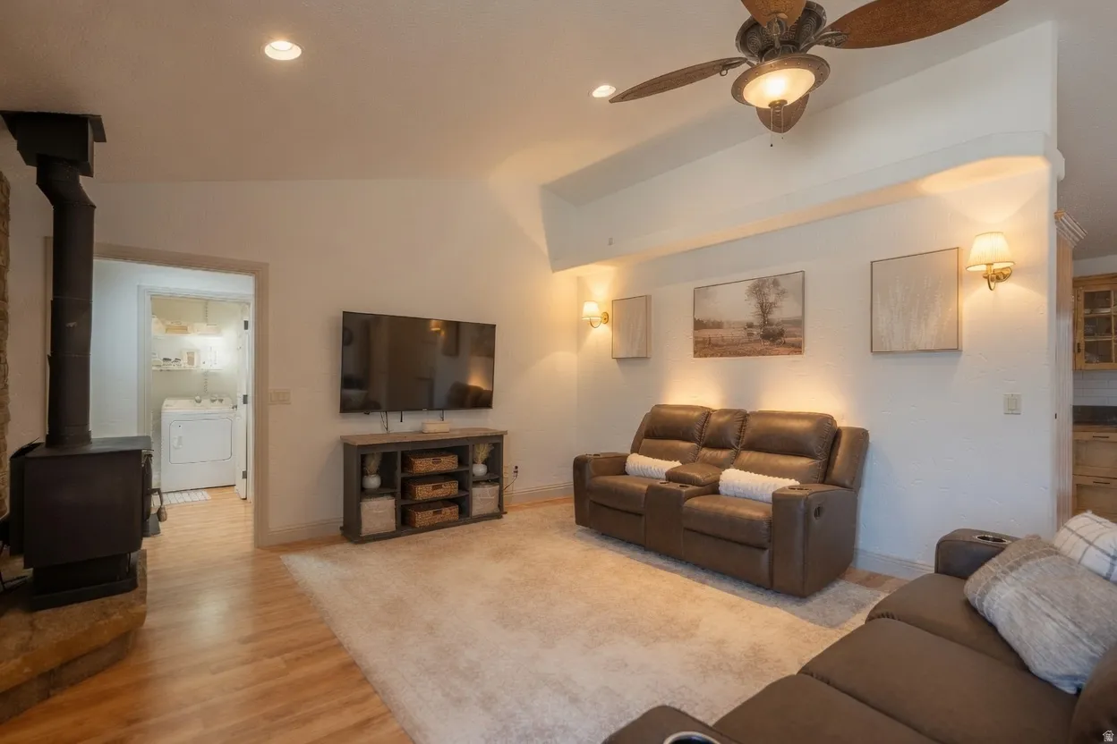 Spacious living area featuring wood-finish flooring, a ceiling fan with integrated lighting, recessed lighting, and wall-mounted sconces