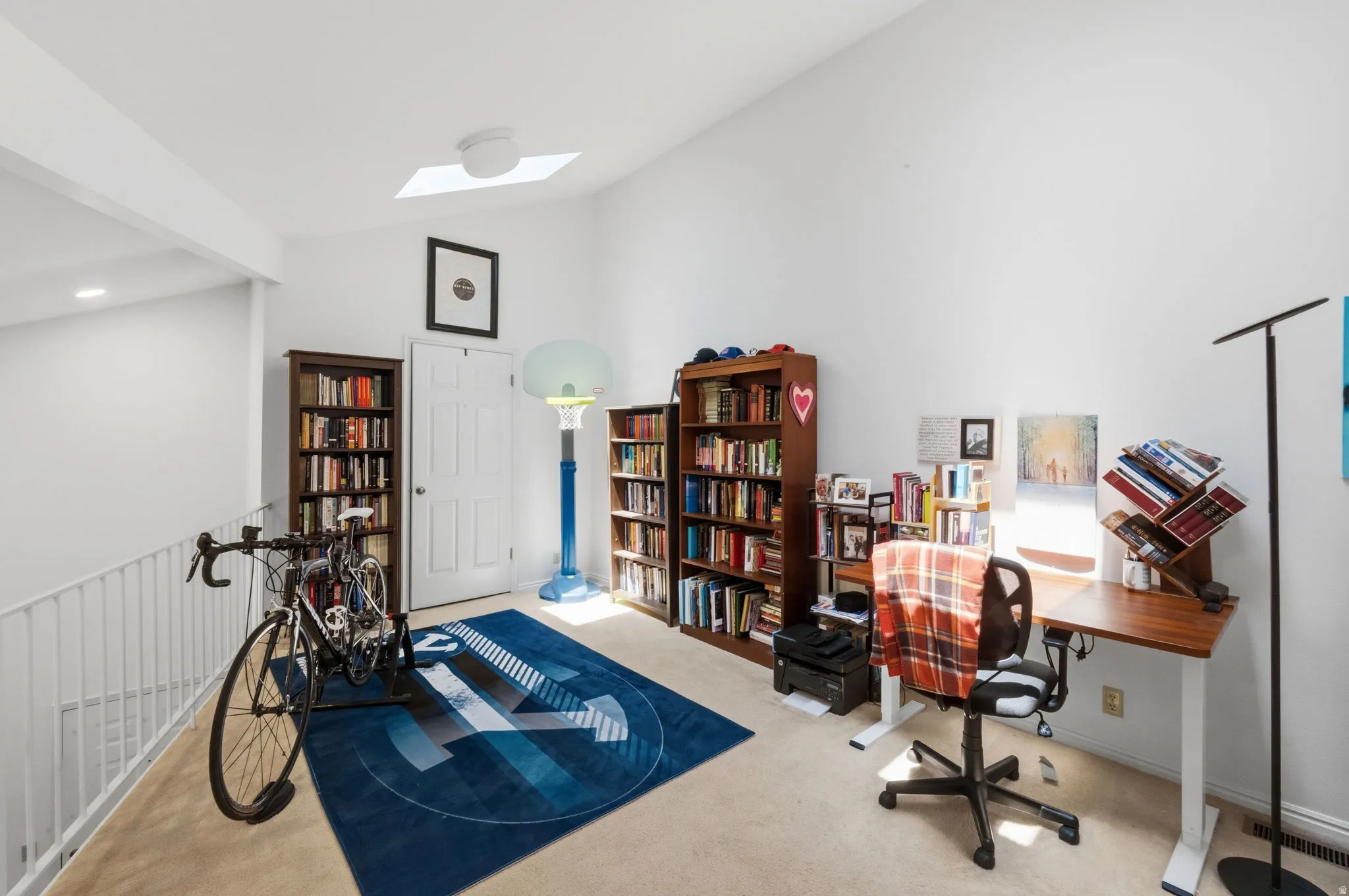 Spacious loft area featuring a vaulted ceiling with a skylight, light-toned carpet flooring, a white interior door, white painted walls, and an open railing overlooking the level below