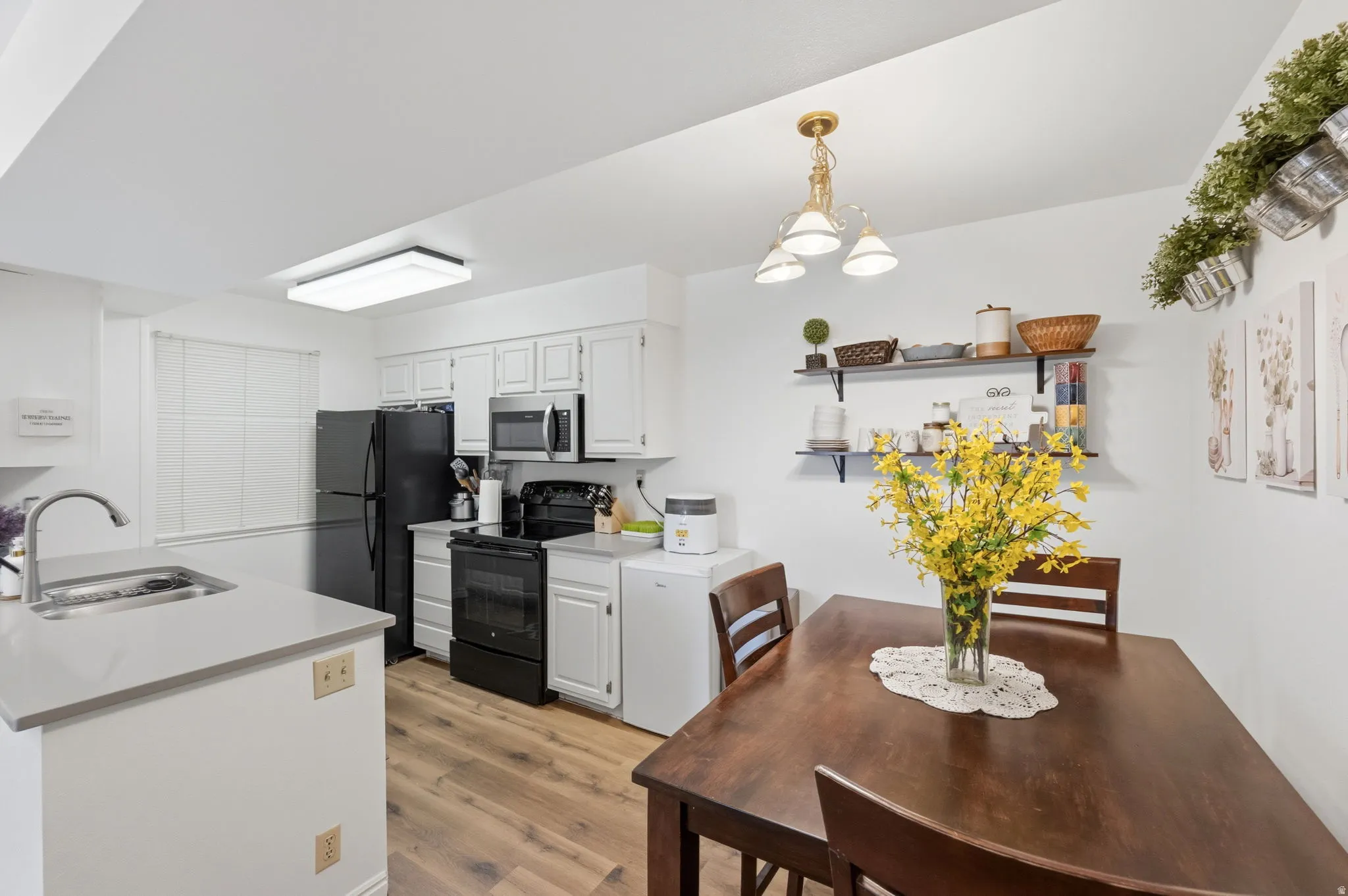 Kitchen and dining area featuring wood-finish flooring, white cabinetry, and black appliances