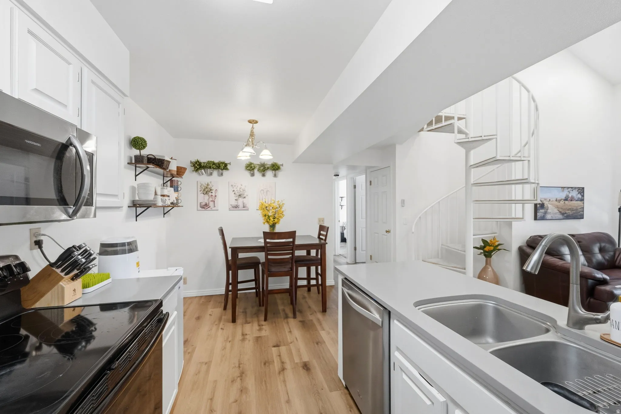Kitchen and dining area featuring stainless steel appliances, wood-finish flooring, a double basin sink, and a spiral staircase