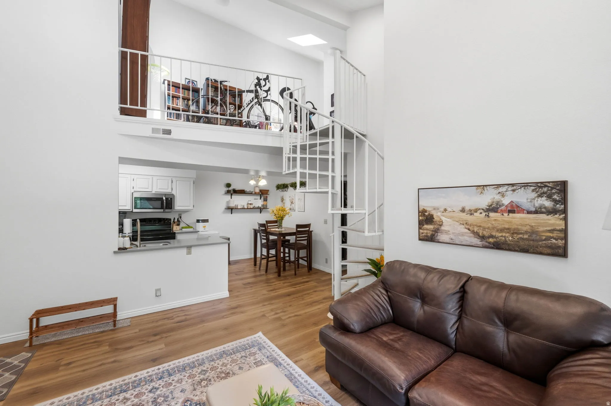 Loft-style living area featuring a spiral staircase, wood-finish flooring, a kitchen pass-through, and a vaulted ceiling with a skylight