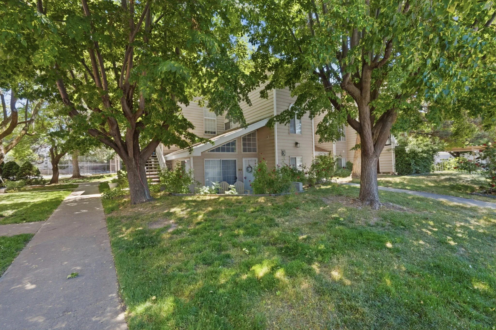 Two-story siding exterior featuring prominent gabled entryway, ground-level sliding glass door, mature shade trees, and a concrete pathway
