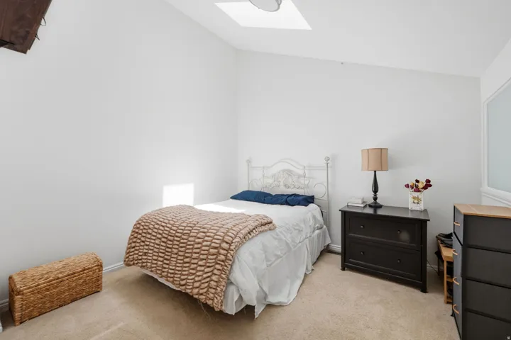 Carpeted room featuring a white painted vaulted ceiling, a skylight, and white walls
