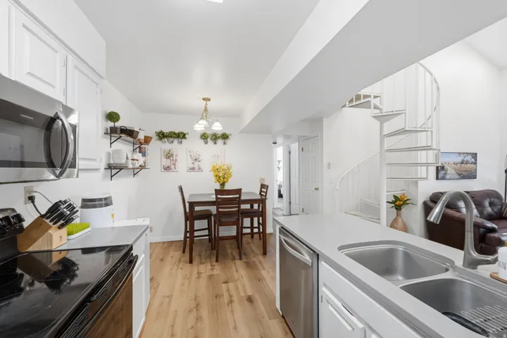 Kitchen and dining area featuring stainless steel appliances, wood-finish flooring, a double basin sink, and a spiral staircase
