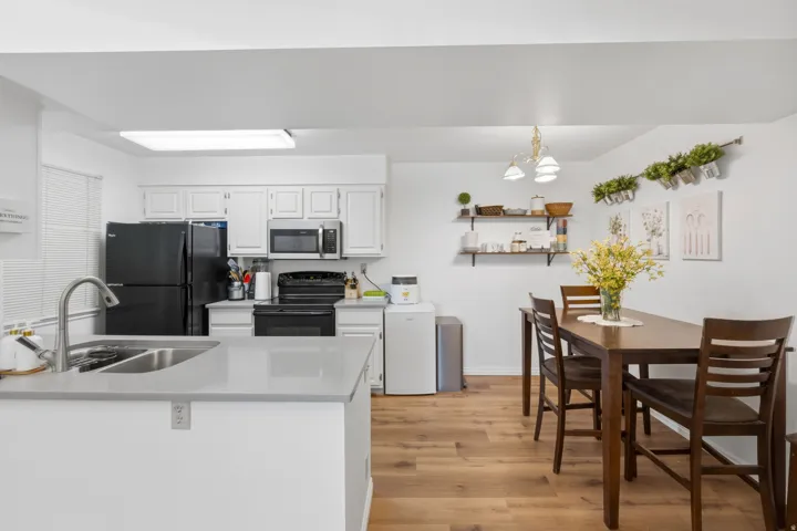 Kitchen featuring light gray countertops, white cabinetry, black appliances, a double basin sink with a gooseneck faucet, and wood-finish flooring