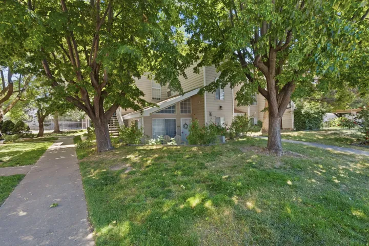 Two-story siding exterior featuring prominent gabled entryway, ground-level sliding glass door, mature shade trees, and a concrete pathway