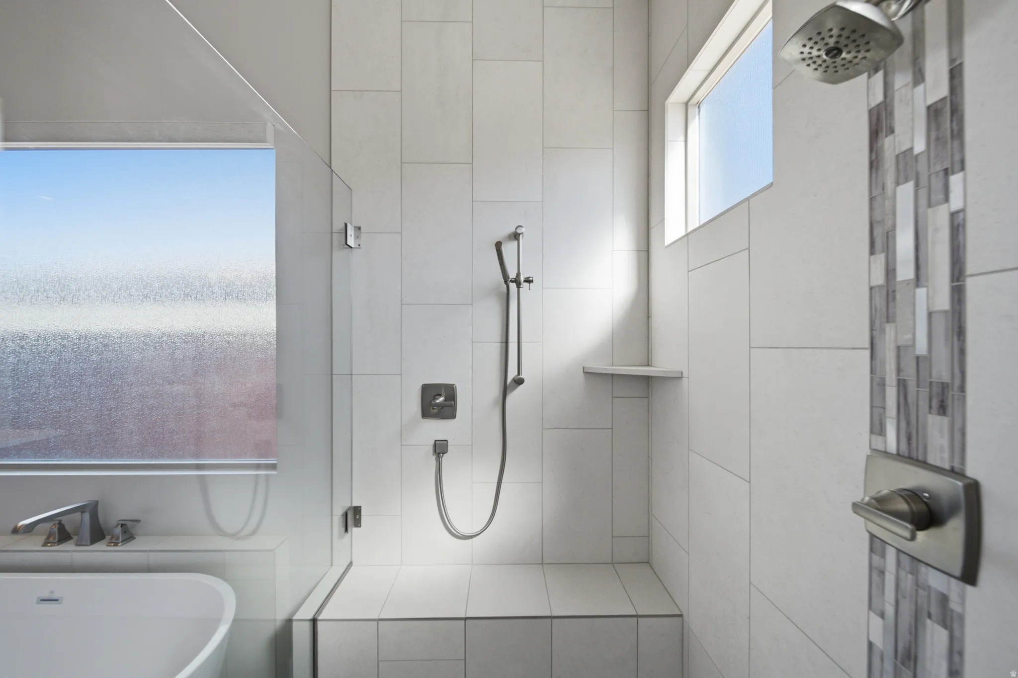 Walk-in shower featuring light-toned tile walls, a built-in bench, and a niche shelf