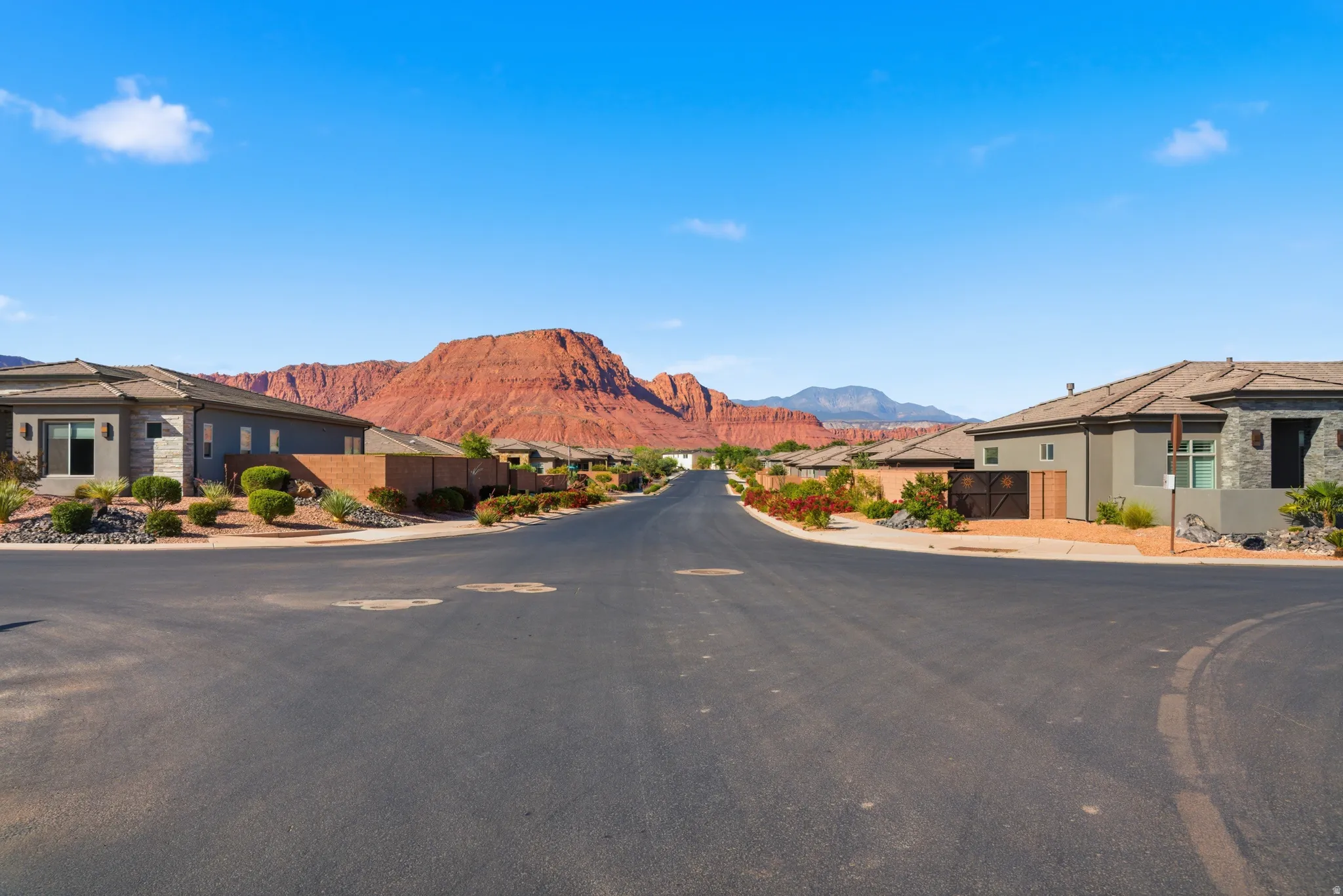 Paved neighborhood street with single-story homes featuring stucco and stone exteriors, and tile roofs